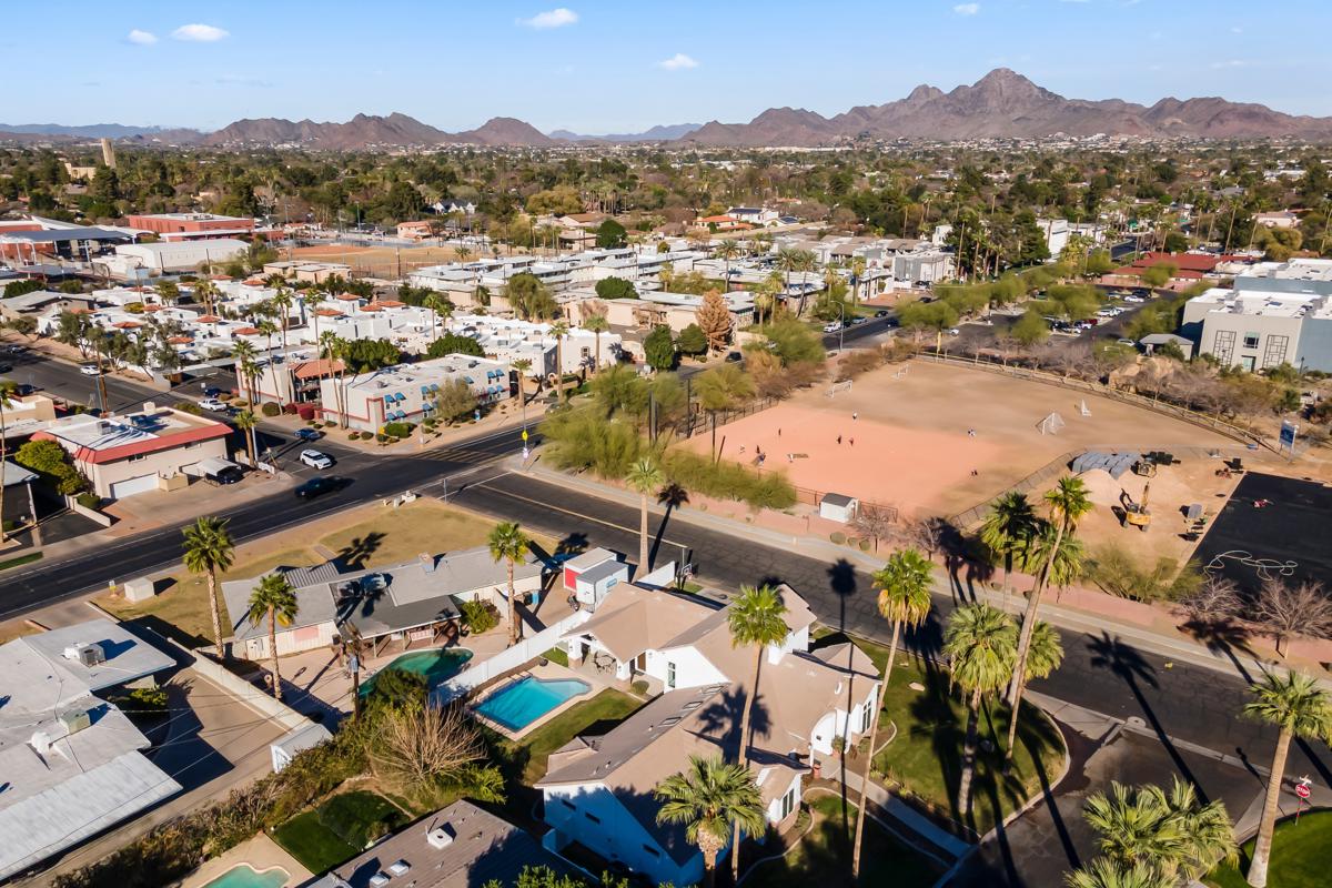 Neighborhood scene with rooftops, a school sports field, and mountain views.