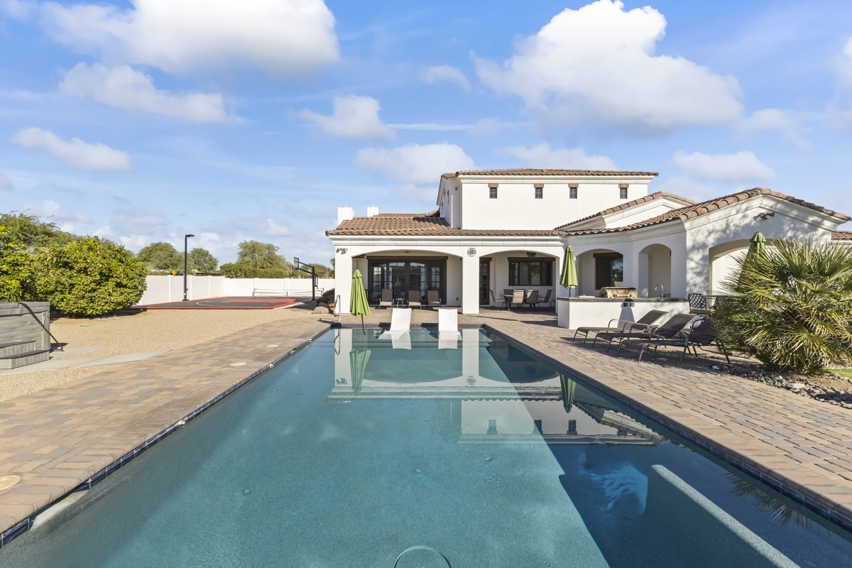 Luxury home with a large pool, patio seating, and Spanish-style architecture.