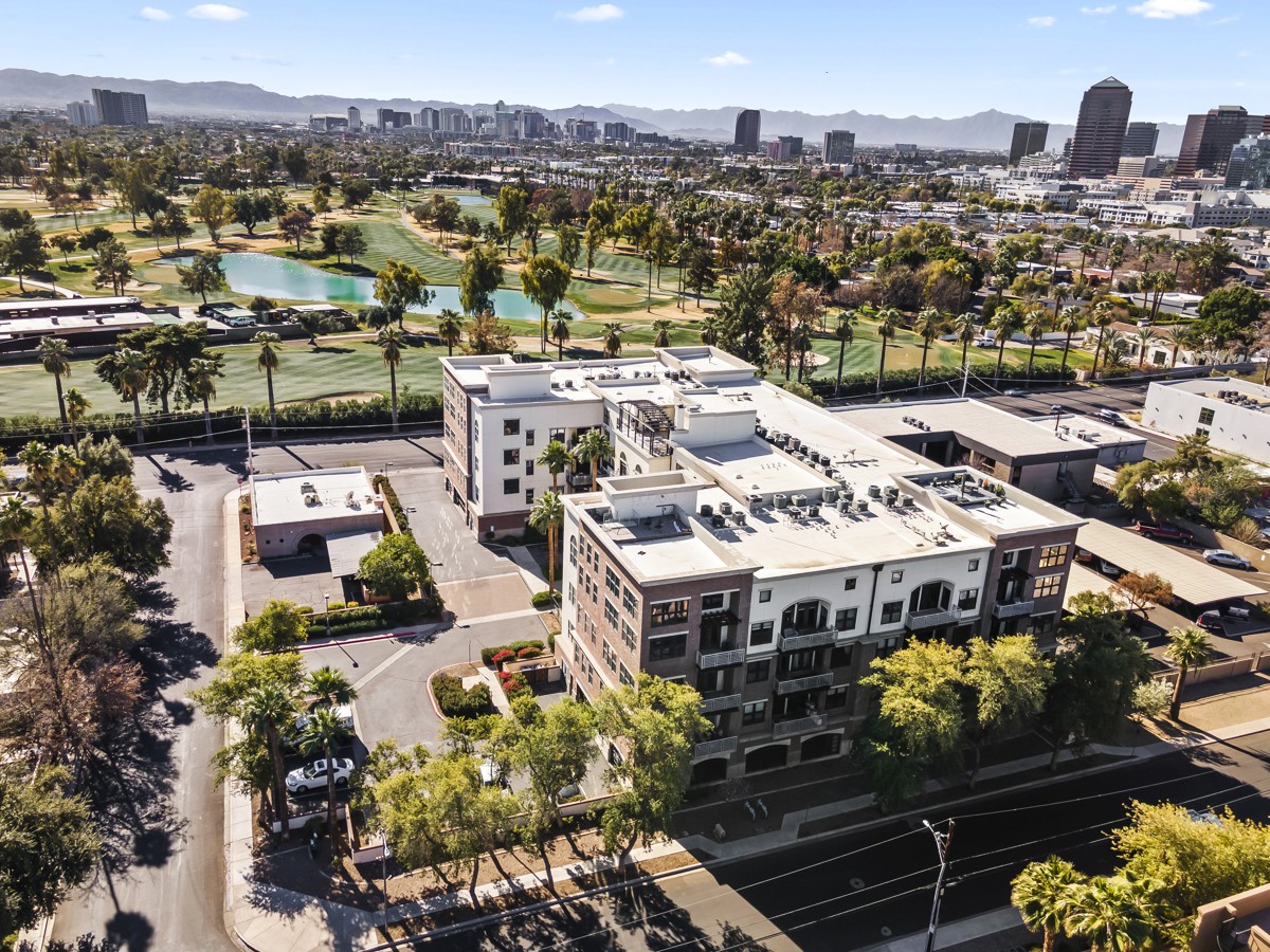 Aerial view of a mid-rise apartment building next to a golf course with the Greater Phoenix skyline in the background.