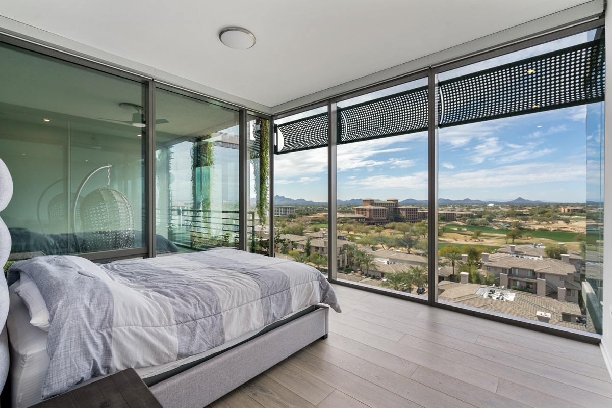 Luxury condo bedroom with floor-to-ceiling windows offering panoramic views of golf course and mountains.