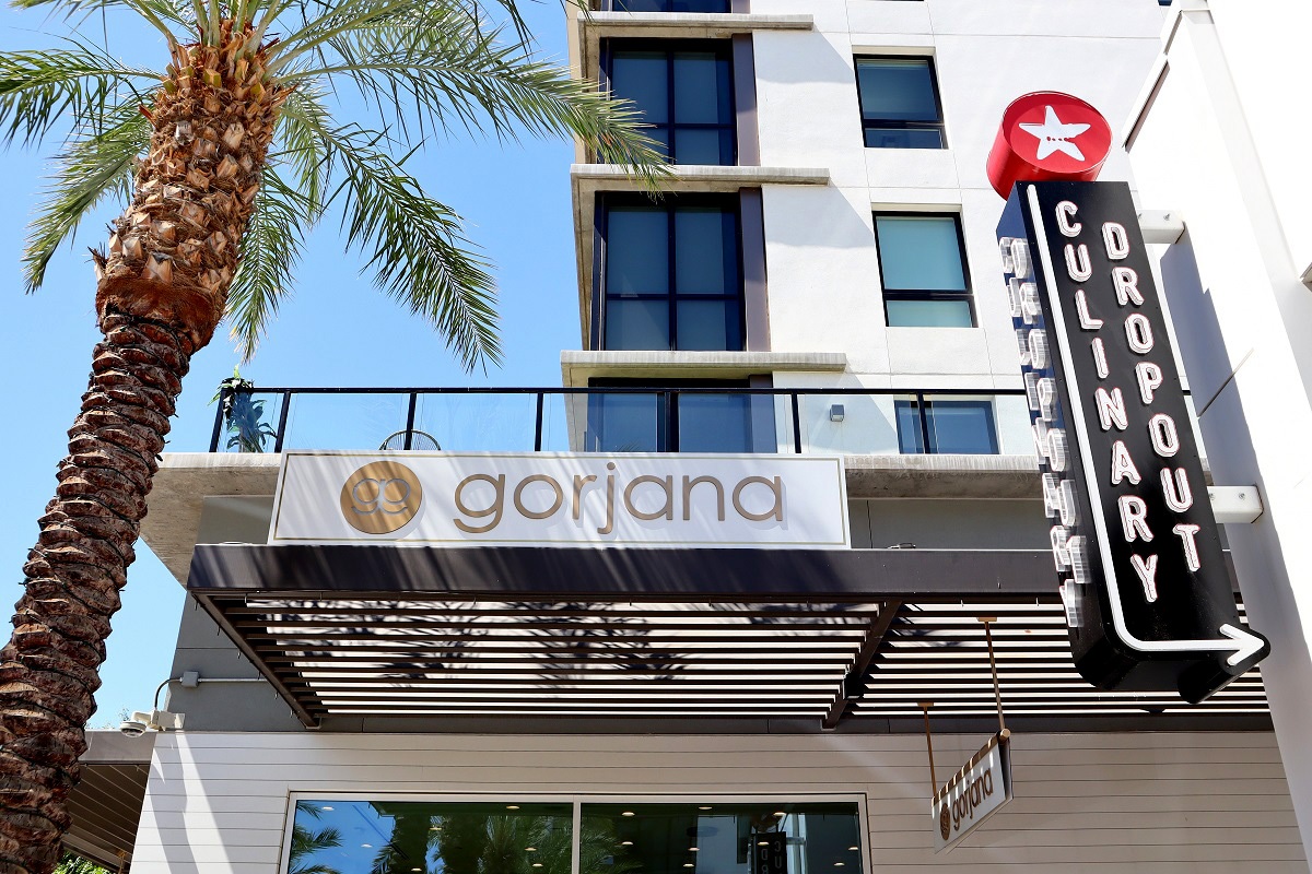 Exterior view of Gorjana jewelry store next to Culinary Dropout restaurant sign with a palm tree.
