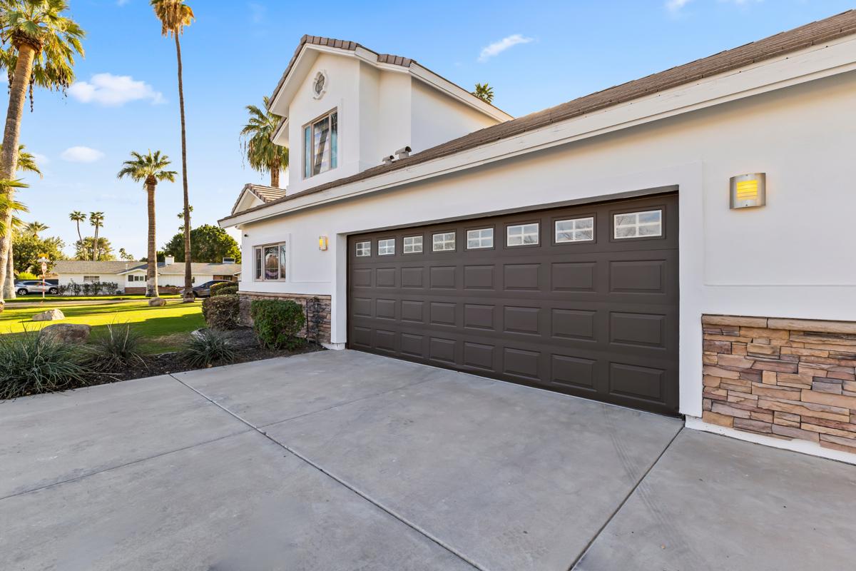 Close-up of a modern two-car garage with brown paneled doors, stone accents, and outdoor wall lights on a clean concrete driveway.