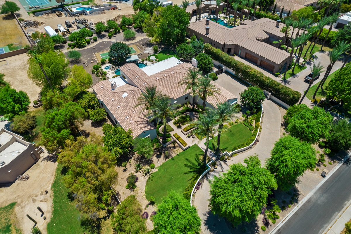 Aerial view of a large desert-style home with landscaped yard, palm trees, and a curved driveway.