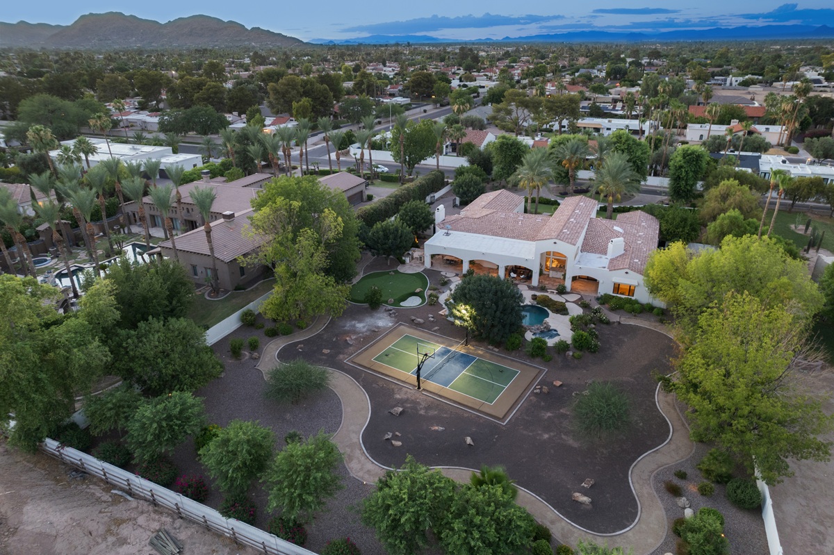 Aerial twilight view of the home, backyard with sport court and pool, and surrounding neighborhood with mountains in the distance.