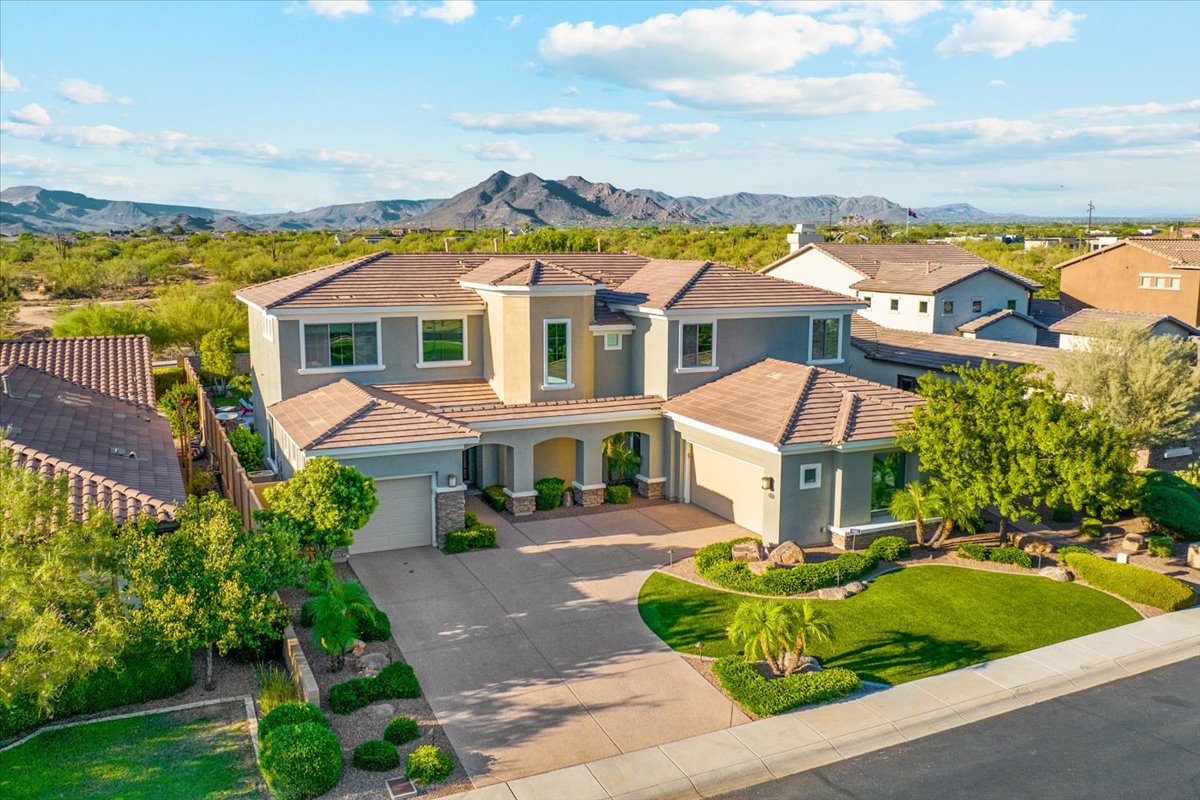 Front view of a large two-story suburban house with a manicured lawn, driveway, and mountains in the background.