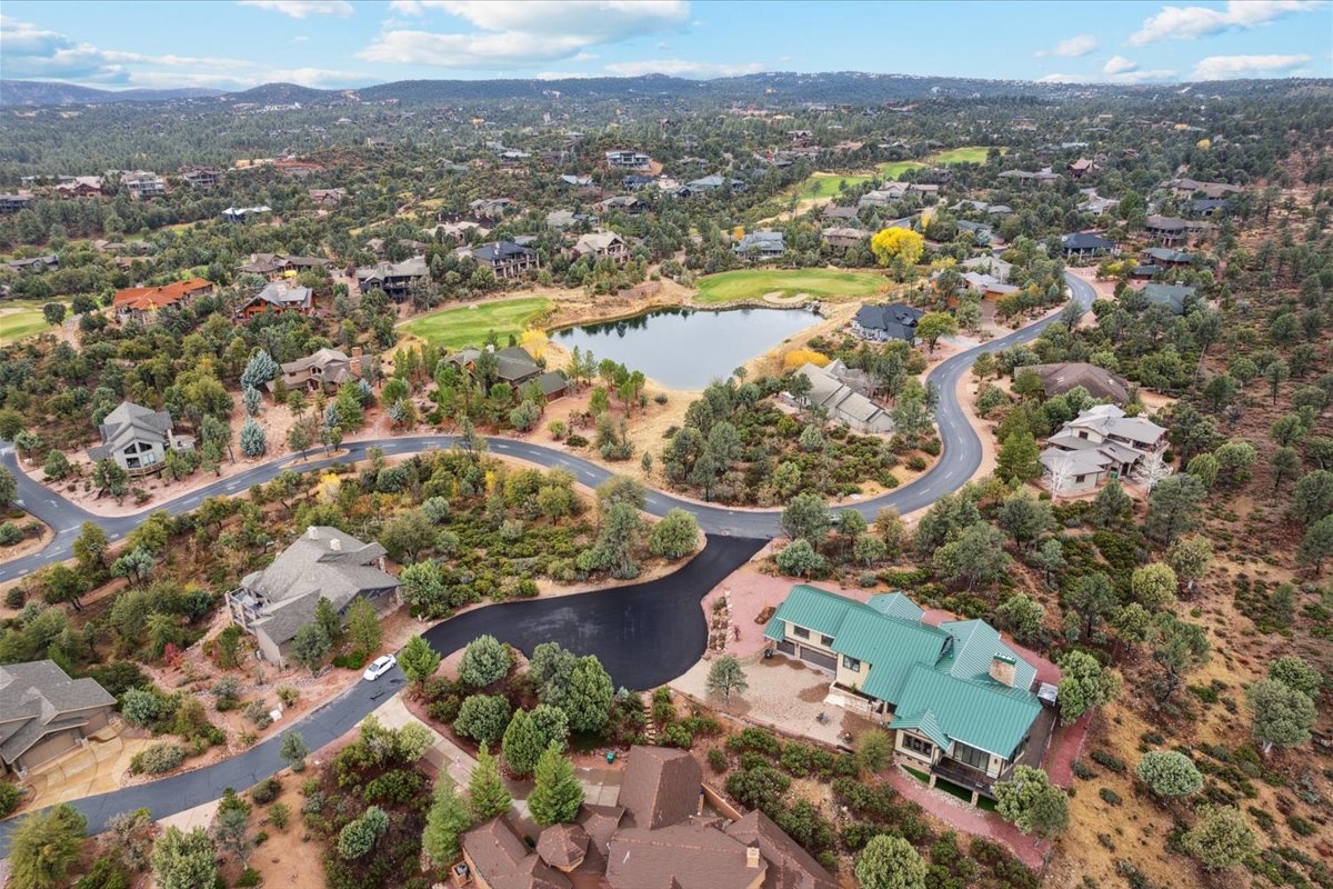 Aerial view of a wooded residential neighborhood with winding roads, scattered homes, and a small lake near the center.