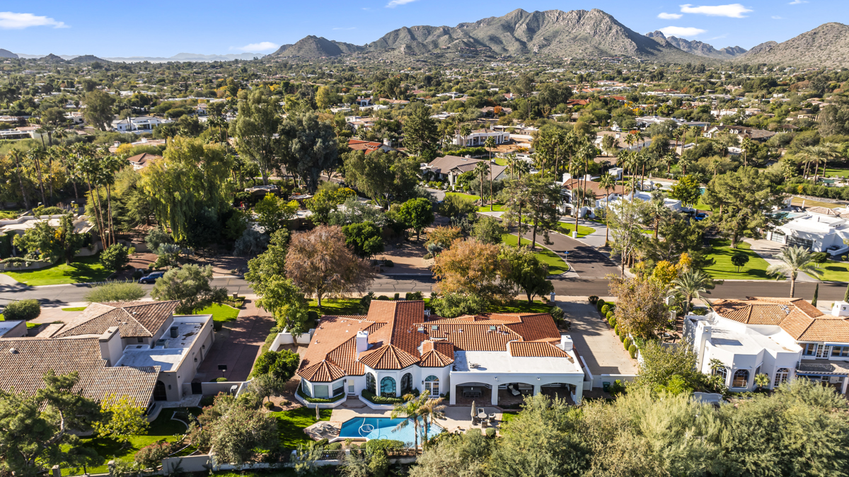 Aerial view of a luxury desert home with a pool, palm trees, and mountains in the background.
