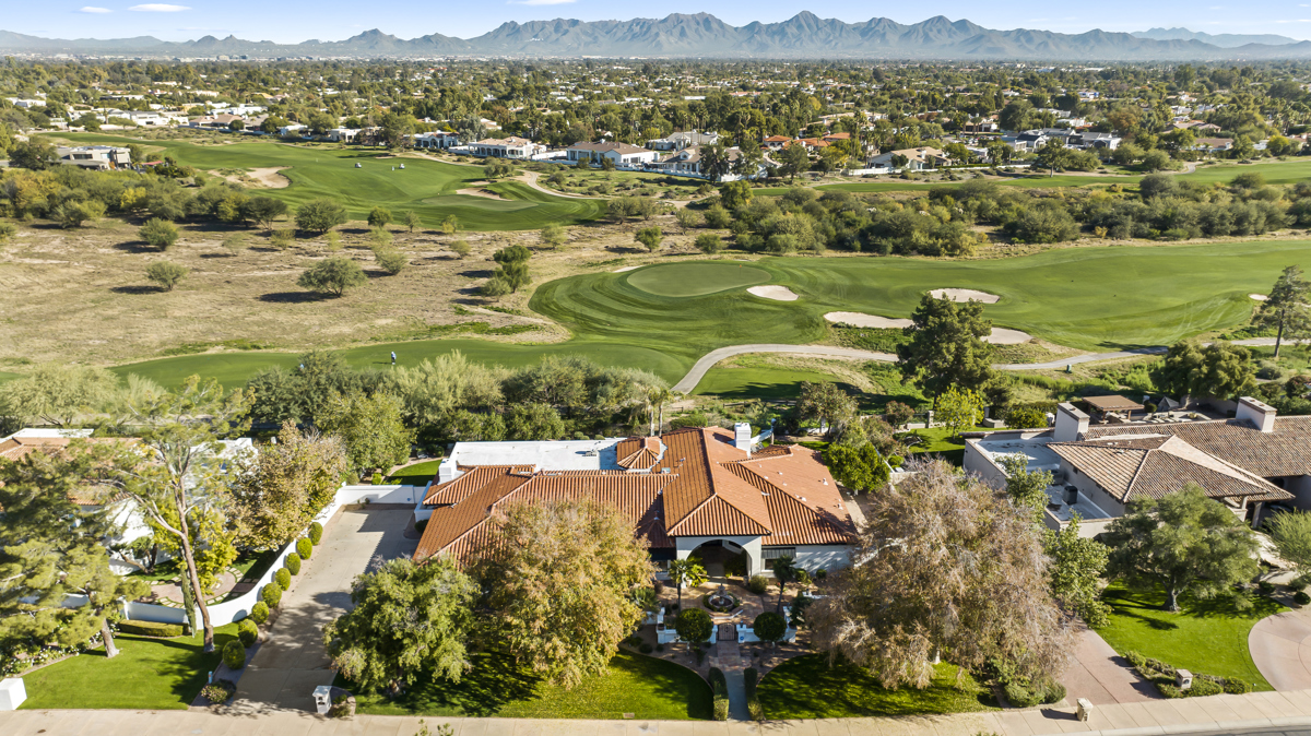 Aerial view of a luxury desert home with a pool, palm trees, and mountains in the background.