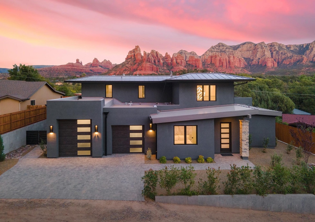 Modern gray home with flat roof set against glowing red rock mountains at sunset.