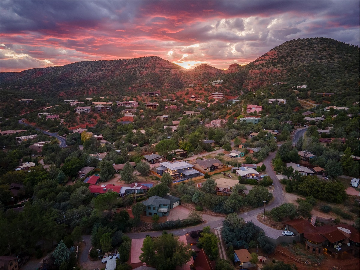 Aerial view of a hillside neighborhood surrounded by red rock terrain and dramatic sunset clouds.