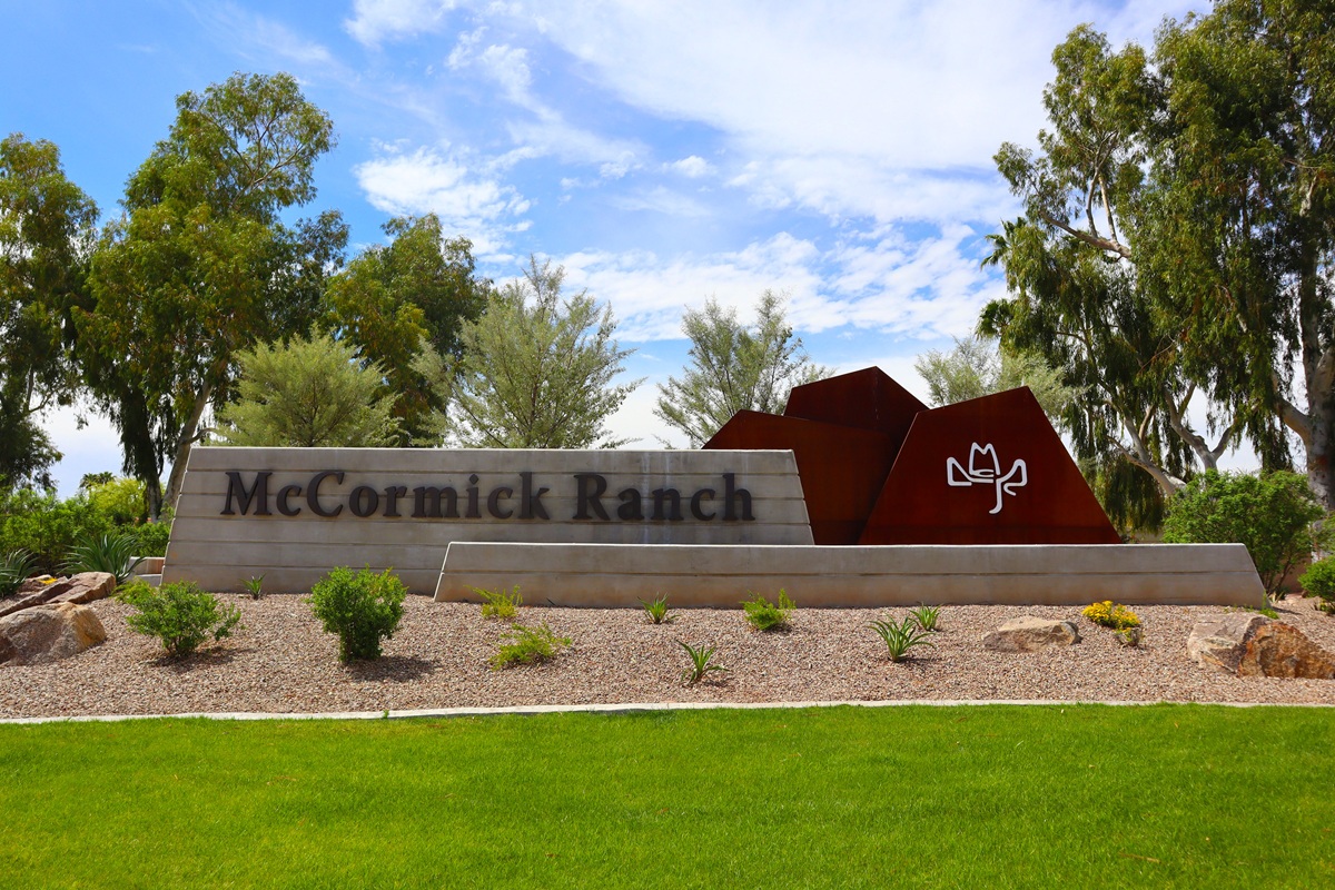 Modern concrete and rusted steel monument sign surrounded by desert landscaping and green grass.