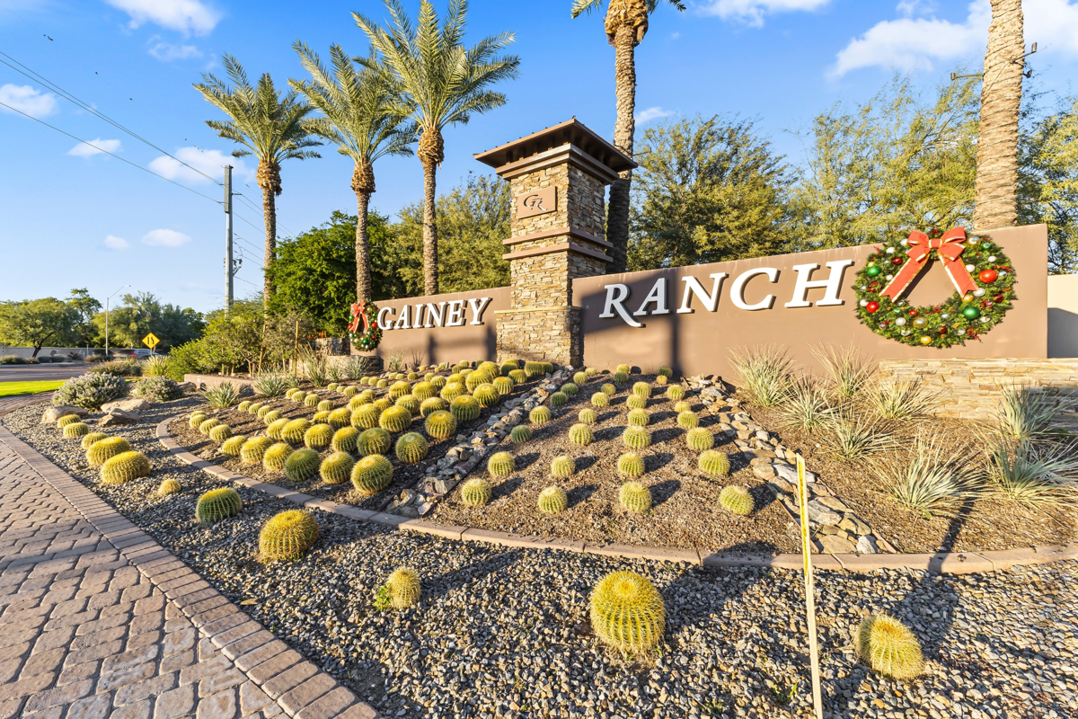 Desert landscape with golden barrel cacti, palm trees, and a “Gainey Ranch” sign decorated with holiday wreaths.
