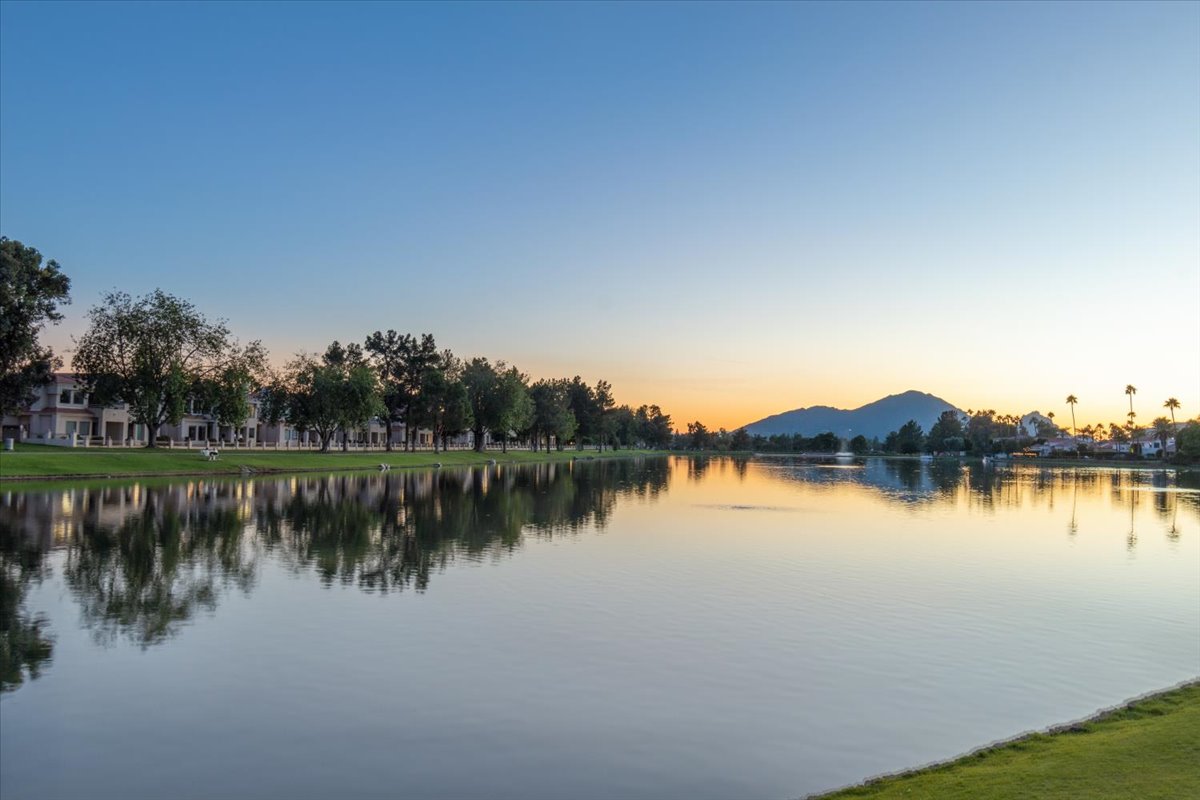 Peaceful lake reflecting trees and homes at sunset, with a mountain in the background.