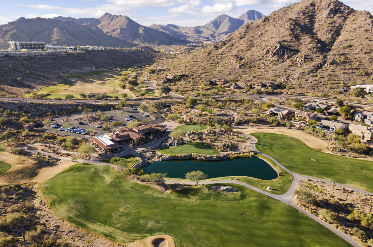 Hillside desert community with modern homes overlooking a golf course and rugged mountains.