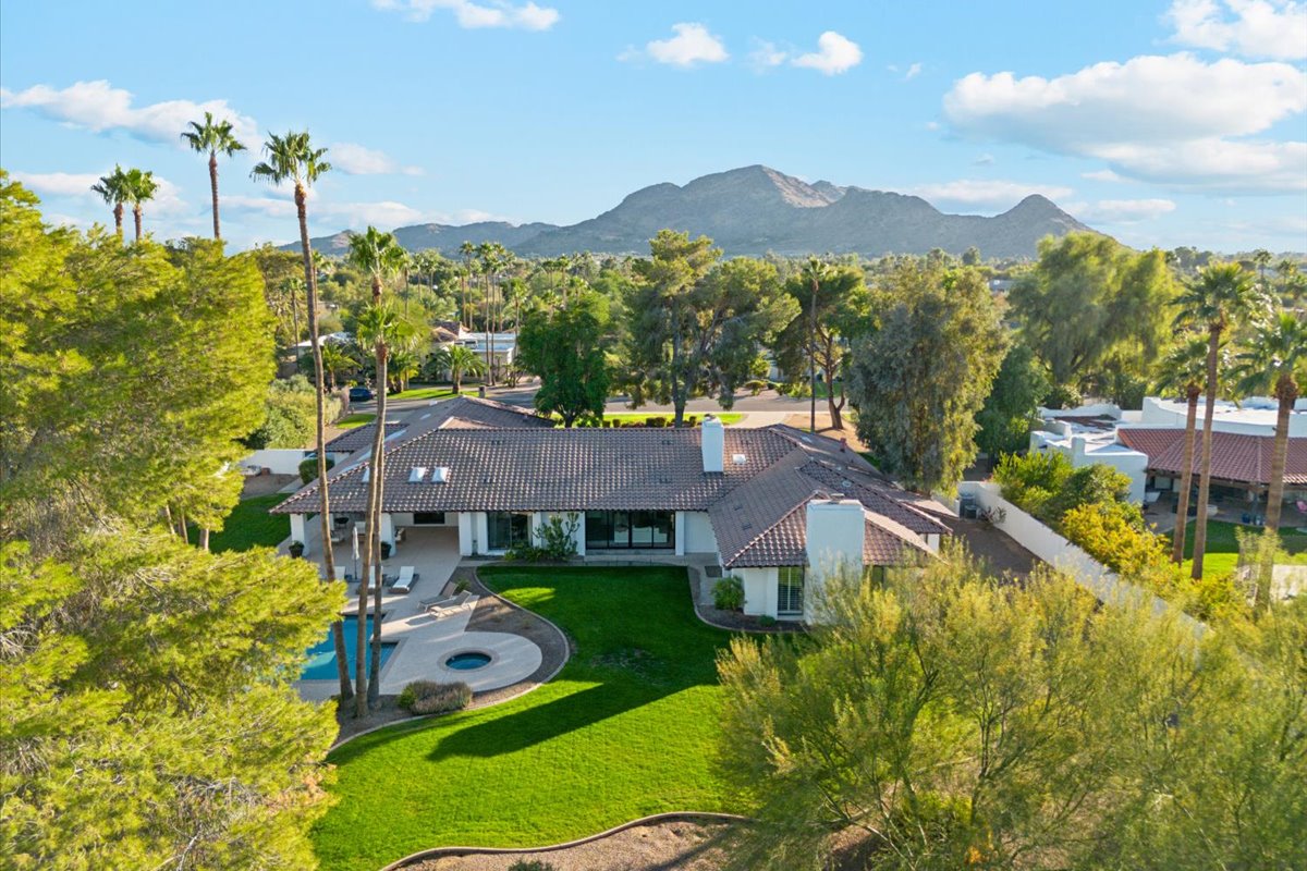 Luxury desert home with palm trees, green lawn, and mountain views in the background.