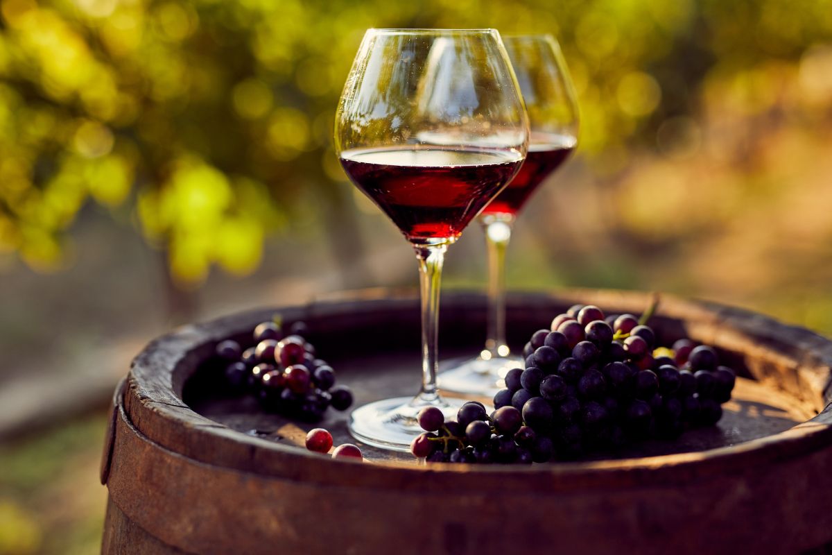 two wine glasses with grapes on barrel