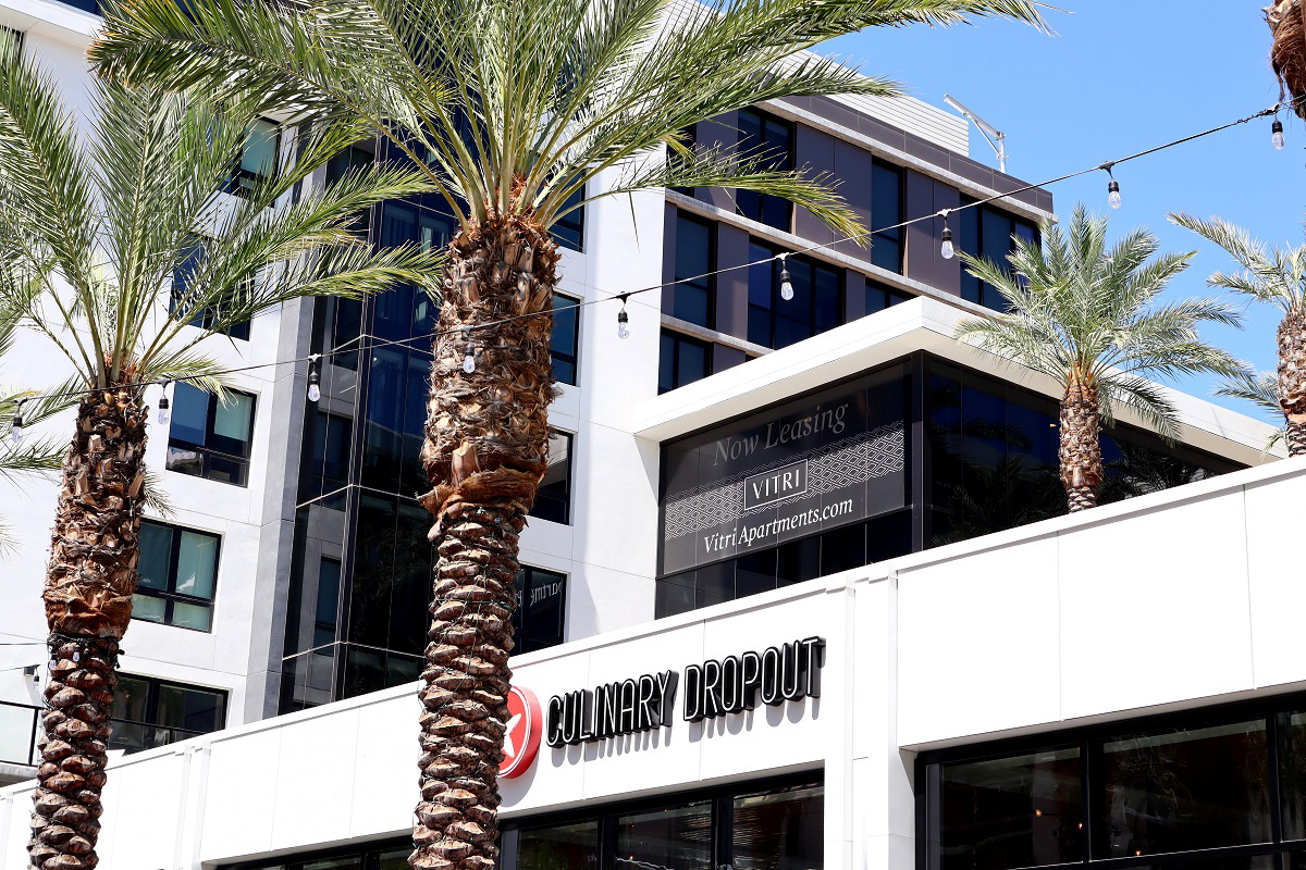 Modern buildings and palm-lined walkways at Scottsdale Quarter, featuring retail spaces and apartments under a clear blue sky.