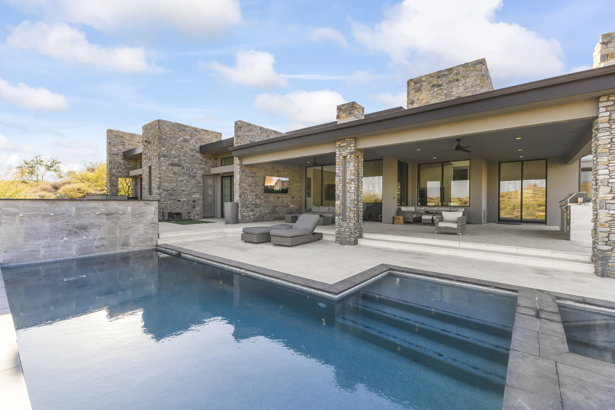 Covered outdoor seating area with stone walls overlooking a rectangular swimming pool and spa.