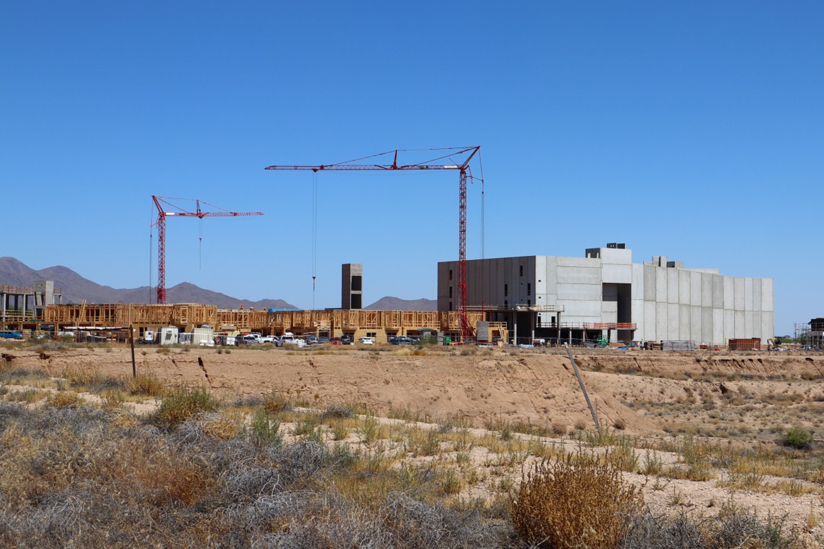 Construction site with cranes building a large structure in a desert landscape.