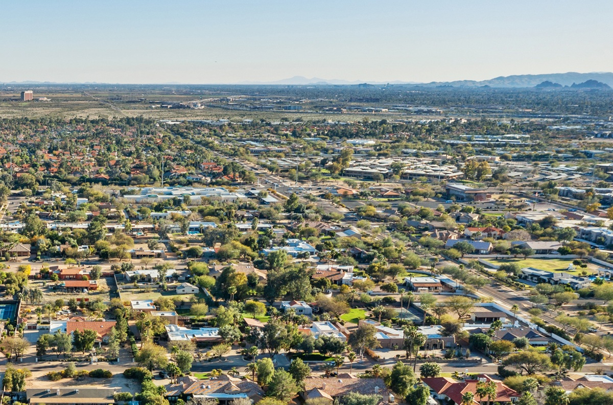 Aerial view of a suburban Phoenix neighborhood with low-rise homes, tree-lined streets, and desert mountains in the distance.