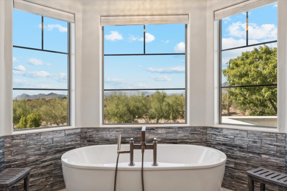 Modern bathroom with a freestanding tub facing large windows overlooking desert vegetation and distant mountains.