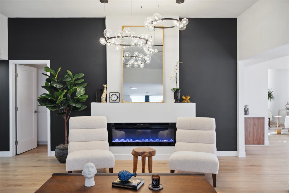 Modern luxury living room with statement chandeliers, fireplace, and black accent wall.