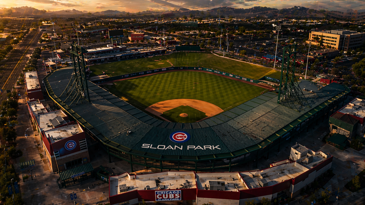 Aerial sunset view of Sloan Park in Mesa, Arizona, showing the Chicago Cubs spring training stadium, green baseball field, surrounding streets, parking lots, and mountain views in the distance.