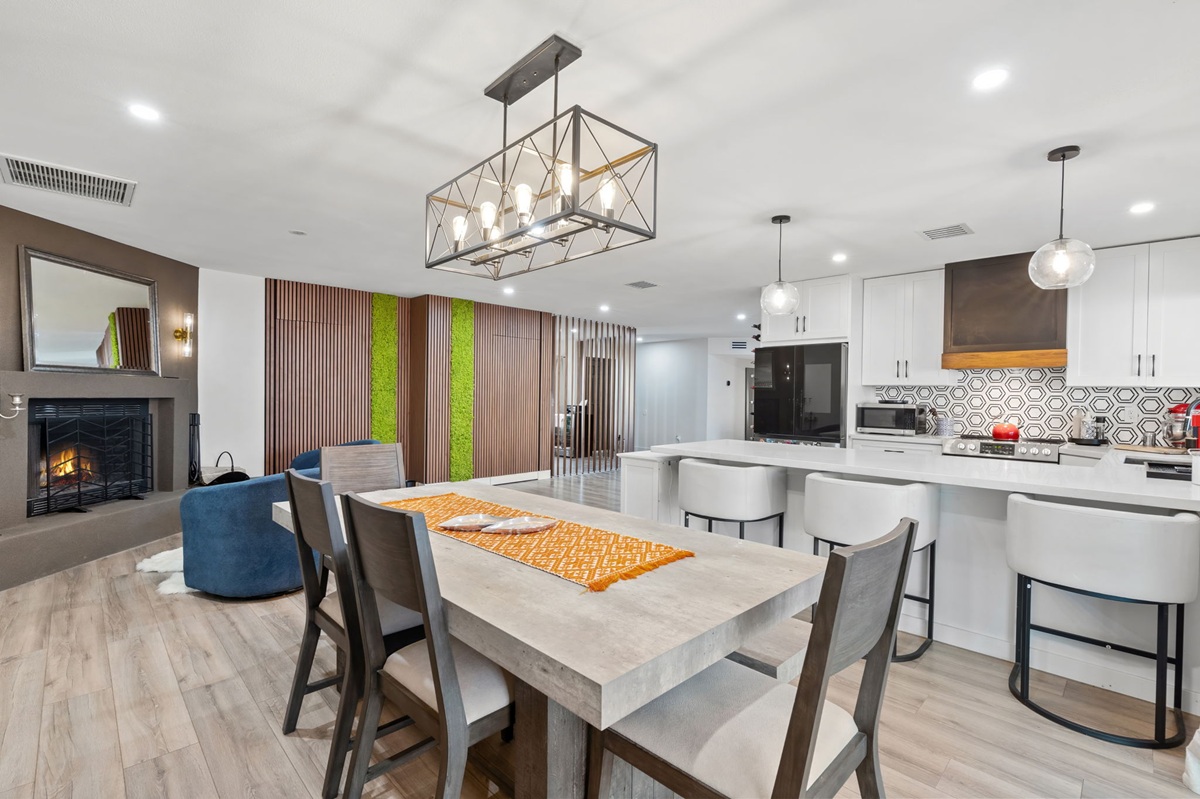 Modern open-plan dining area and kitchen with bar stools, pendant lights, and a fireplace.