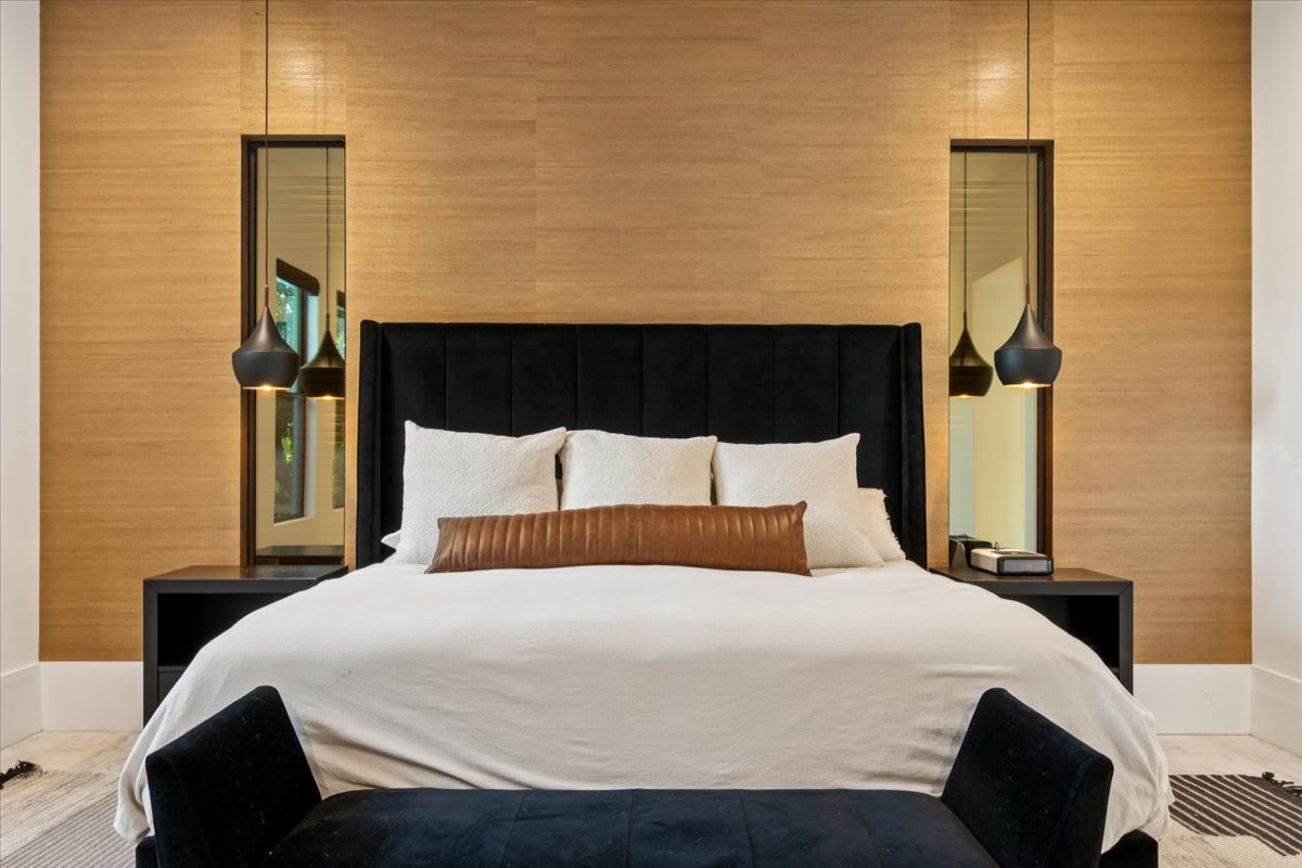 A photo of a modern primary bedroom with a black upholstered bed & warm wood accent wall.