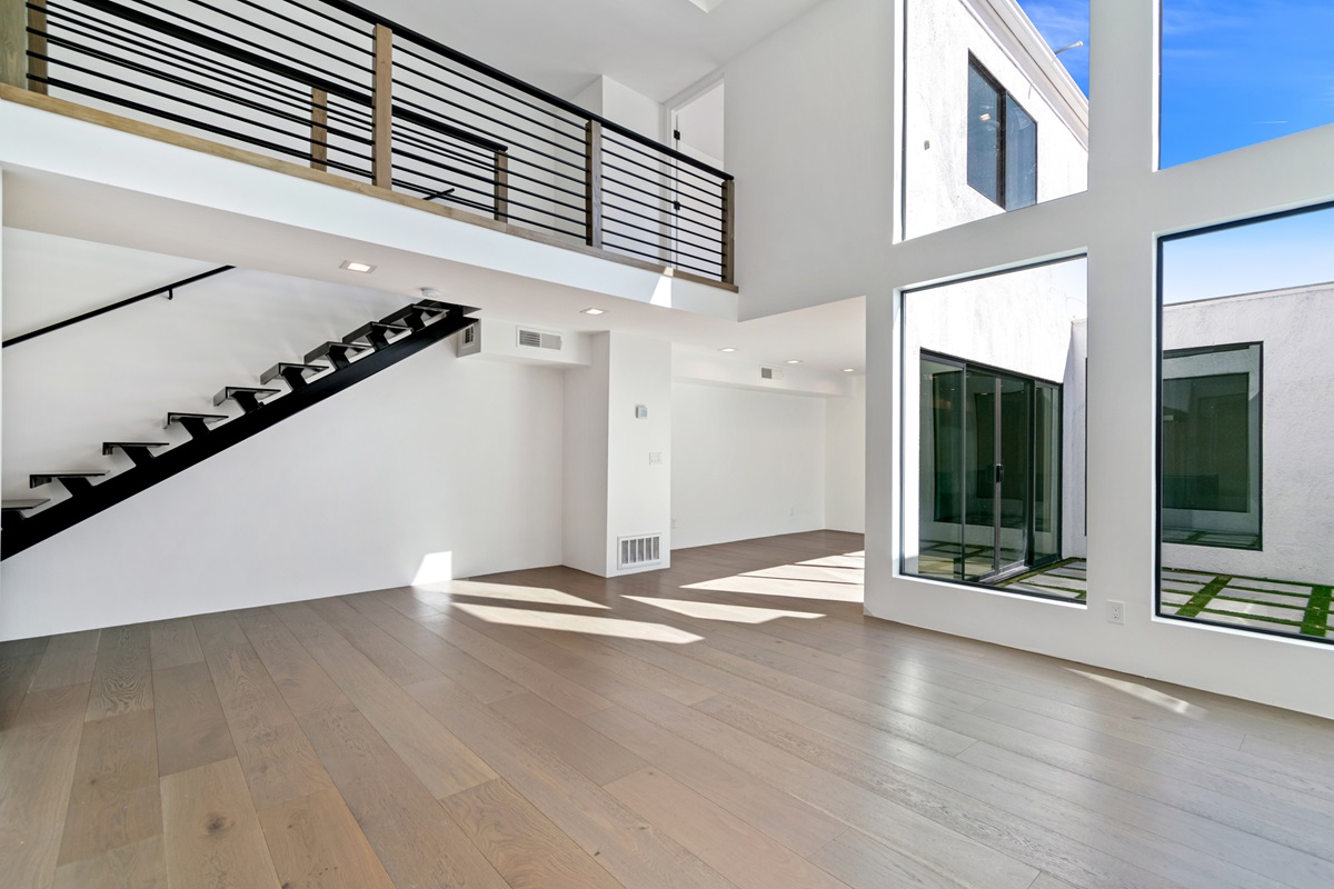 A photo of a bright modern townhome interior with high ceilings, large windows, & a floating staircase.