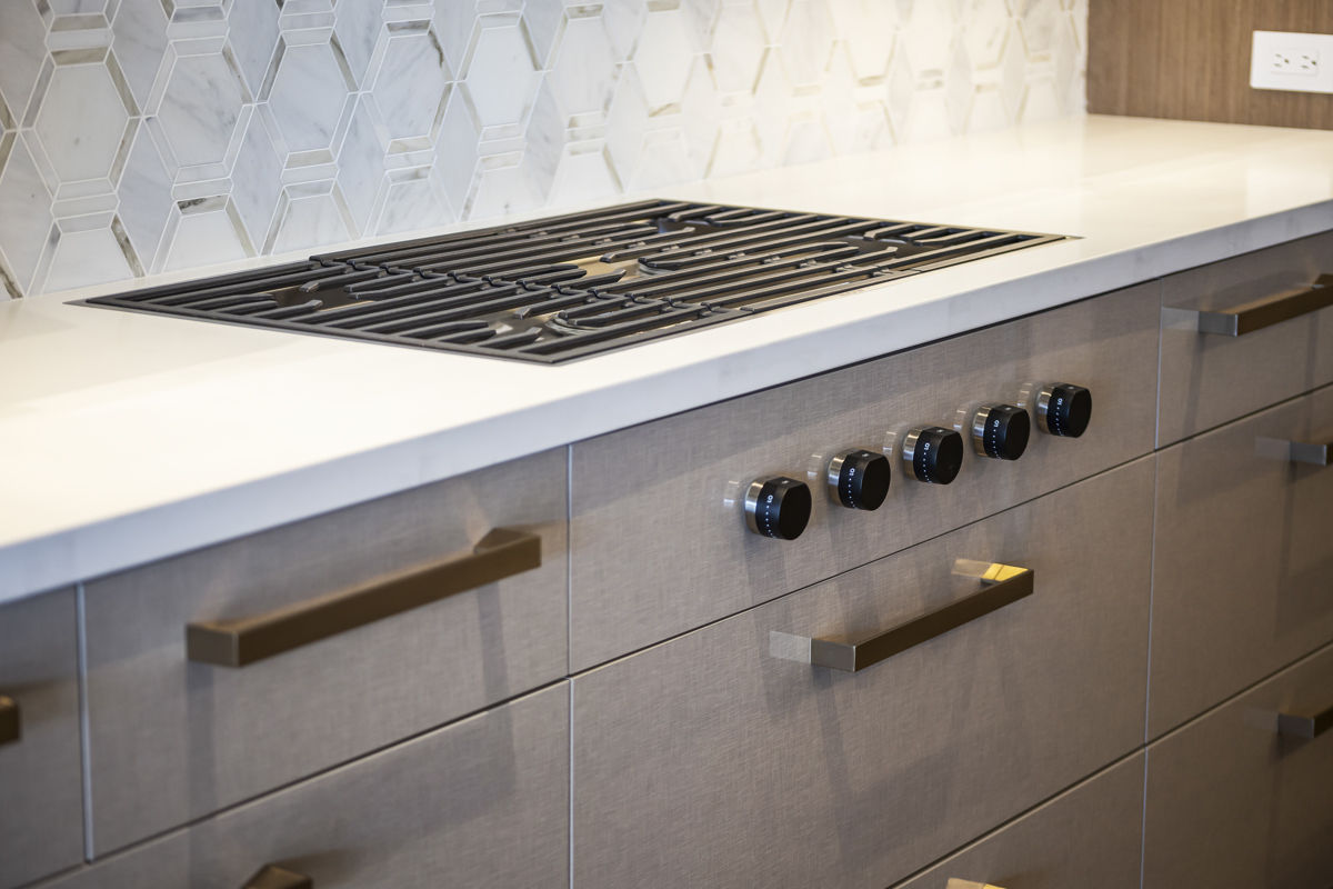 High-end kitchen with a built-in gas cooktop, modern cabinetry, and geometric tile backsplash.