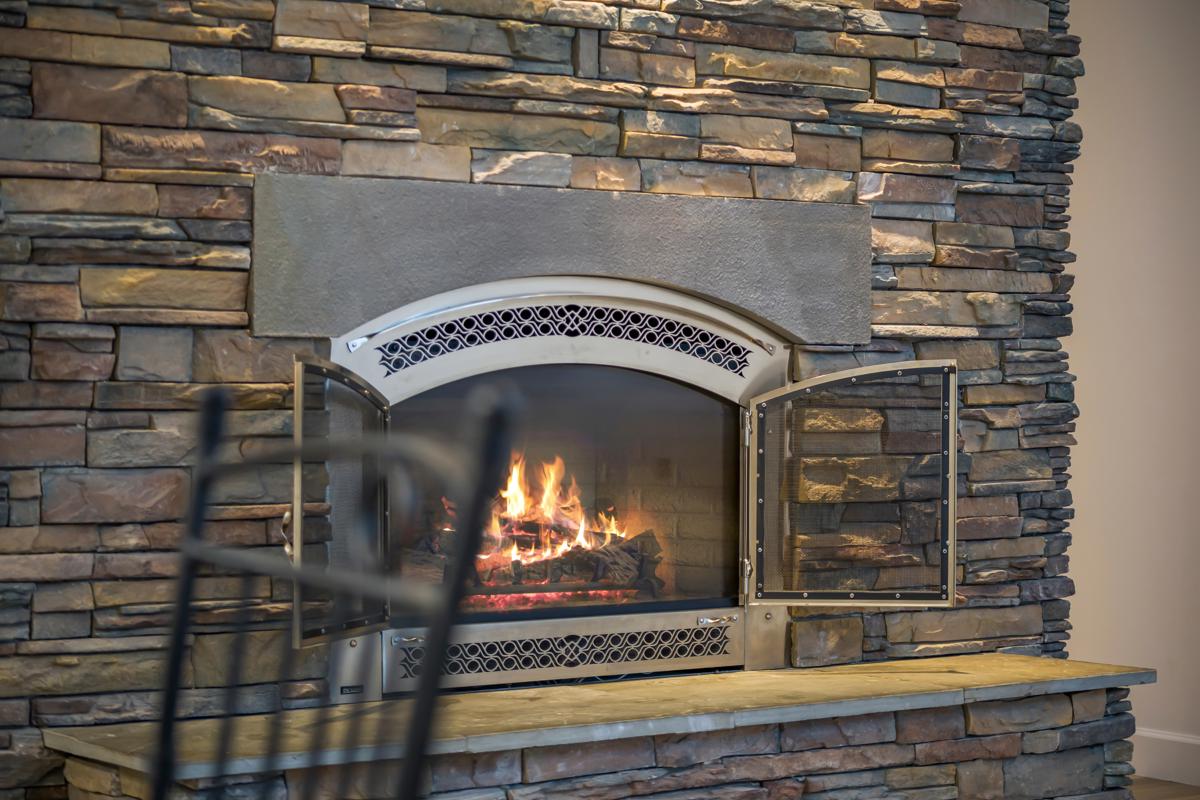 Lit fireplace surrounded by stacked stone inside a luxury home.