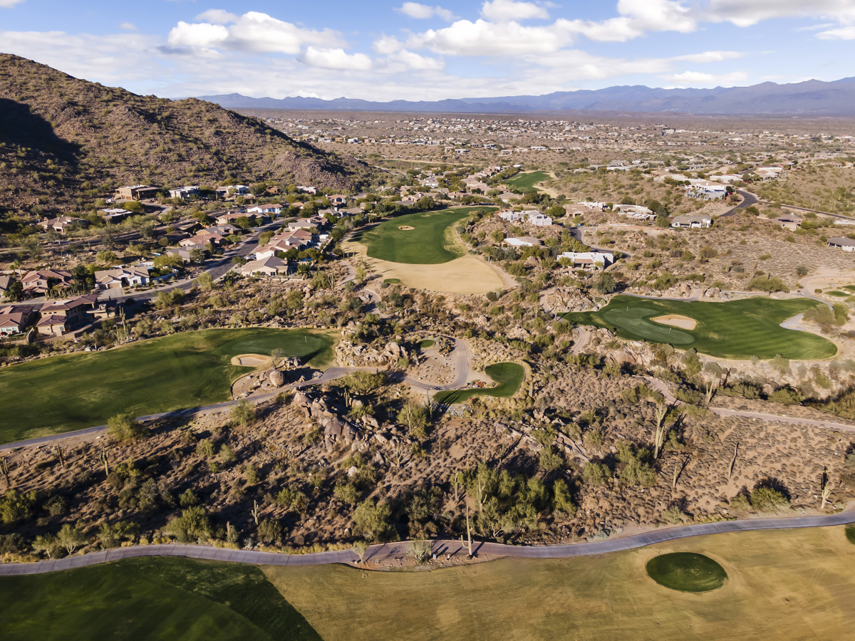 Aerial view of a Scottsdale golf course surrounded by desert homes, mountains, and natural terrain.