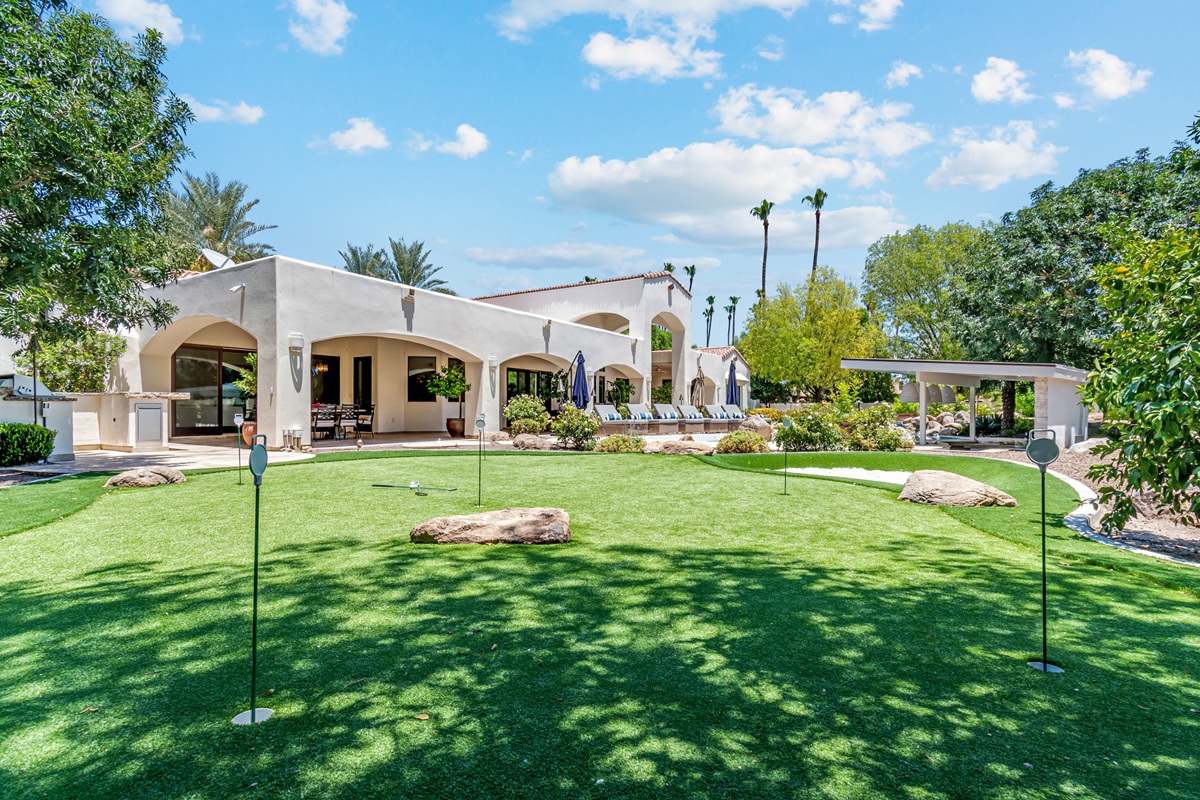 A photo of a Scottsdale backyard with a putting green, large lawn, and a white stucco luxury home.