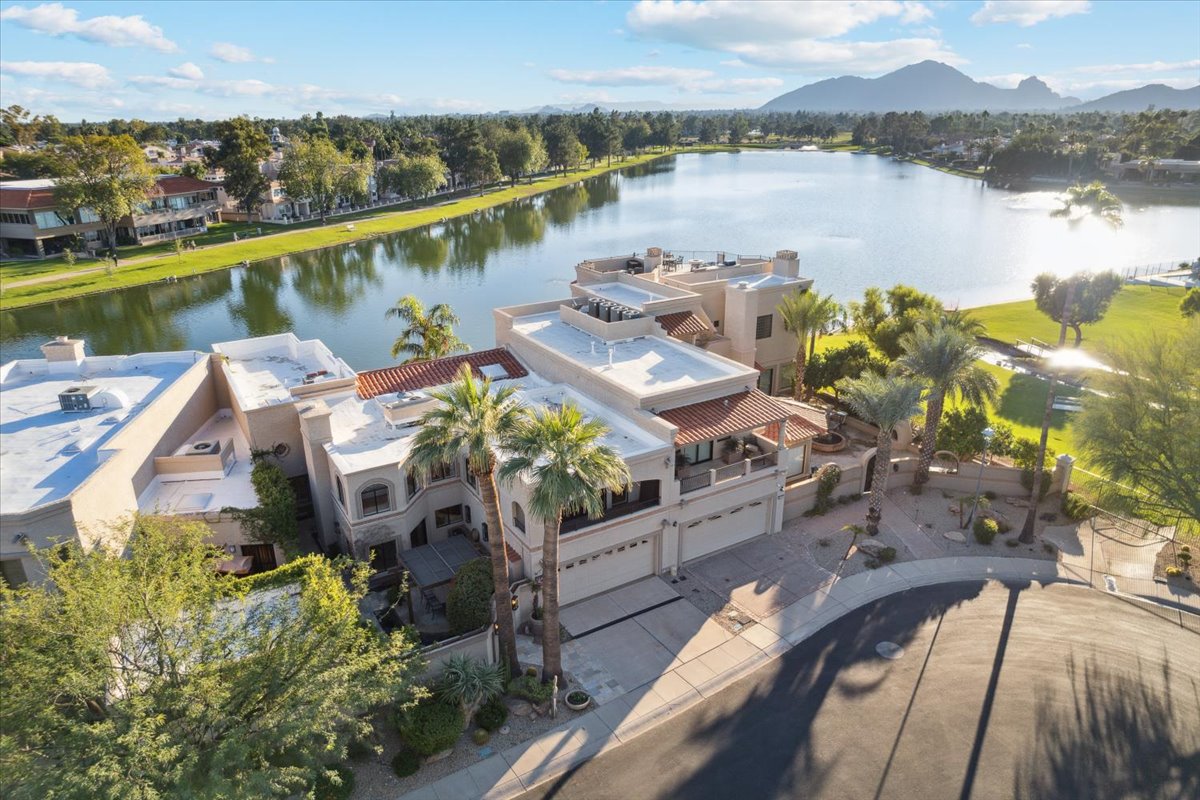 An aerial photo of a luxury waterfront home with palm trees, lake views, and mountain scenery.