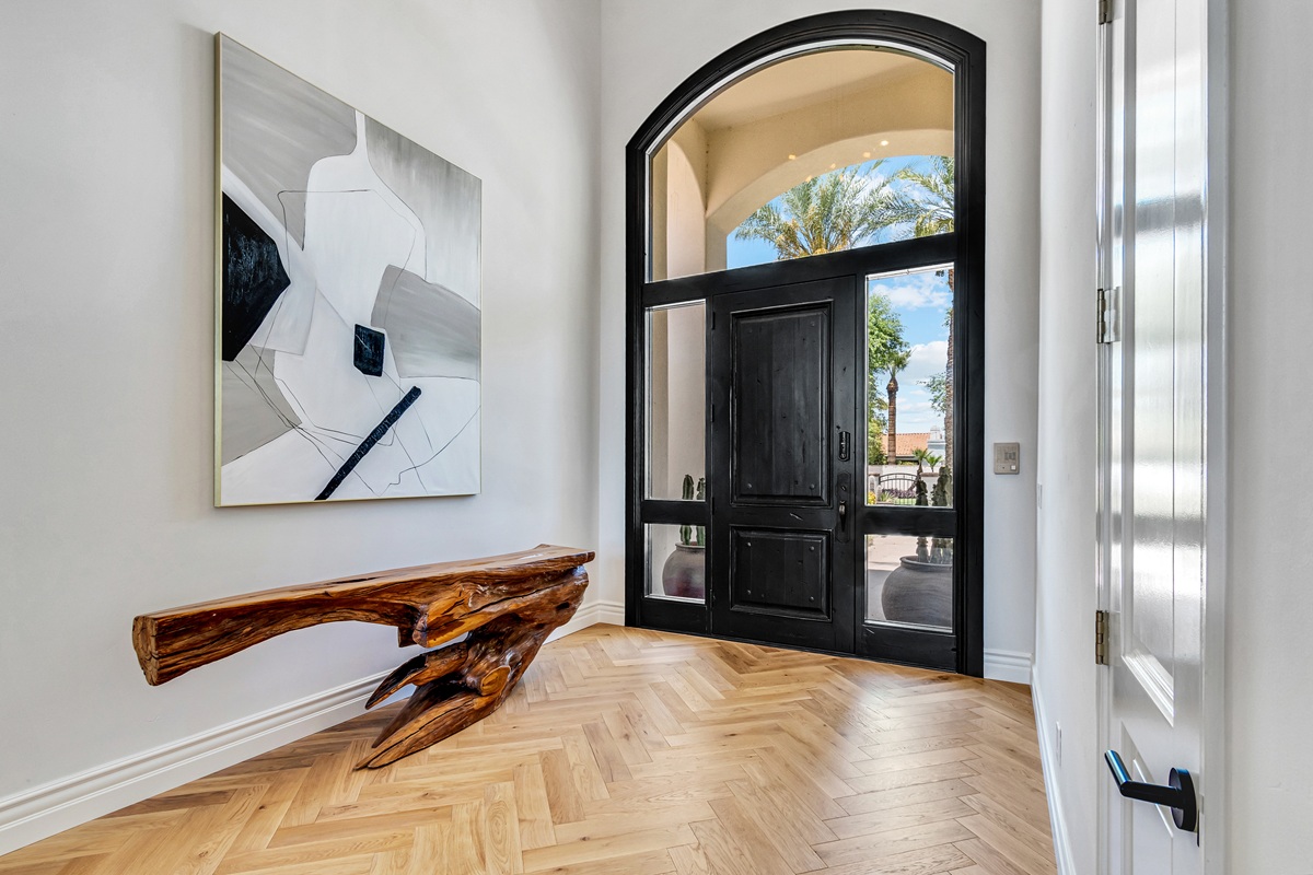Luxury home entry with arched black door and wood flooring.