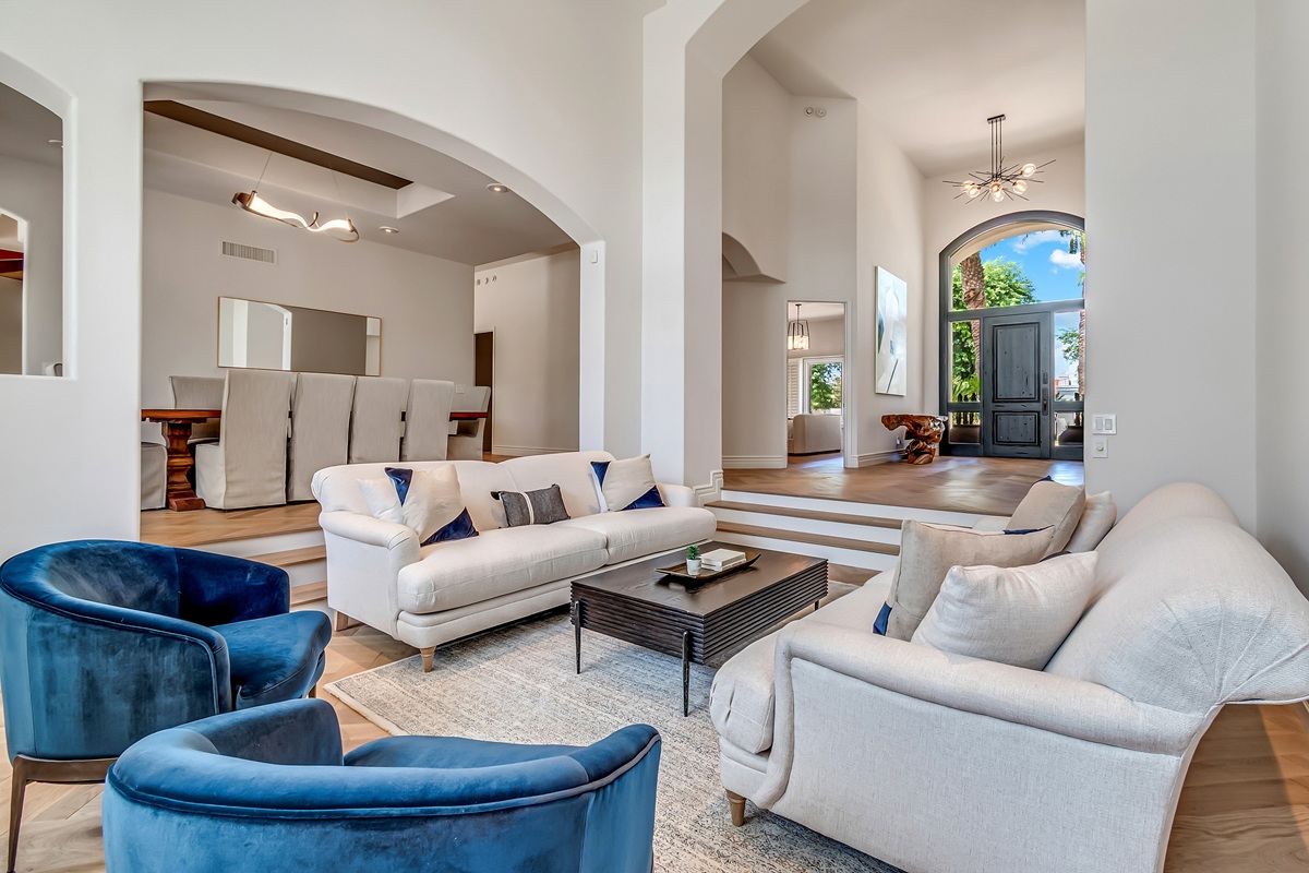 Bright luxury great room with arched architecture, white seating, and blue accent chairs.