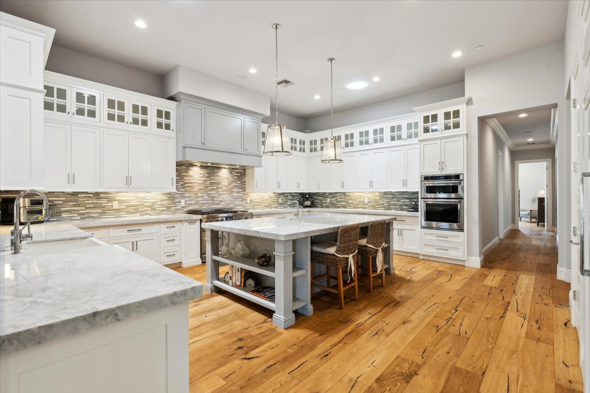 Bright chef’s kitchen with white cabinetry, marble counters, and a large island.