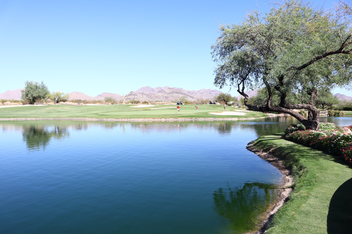Grayhawk golf course with a reflective lake, green fairways, mature desert trees, and mountain views.