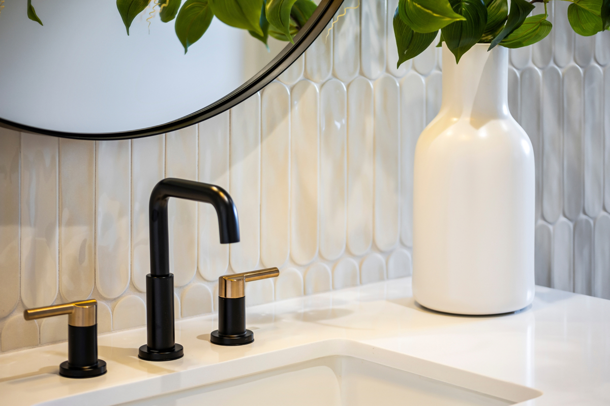 Photo of a designer bathroom sink with matte black and brass fixtures, textured white tile, and modern decorative accents.