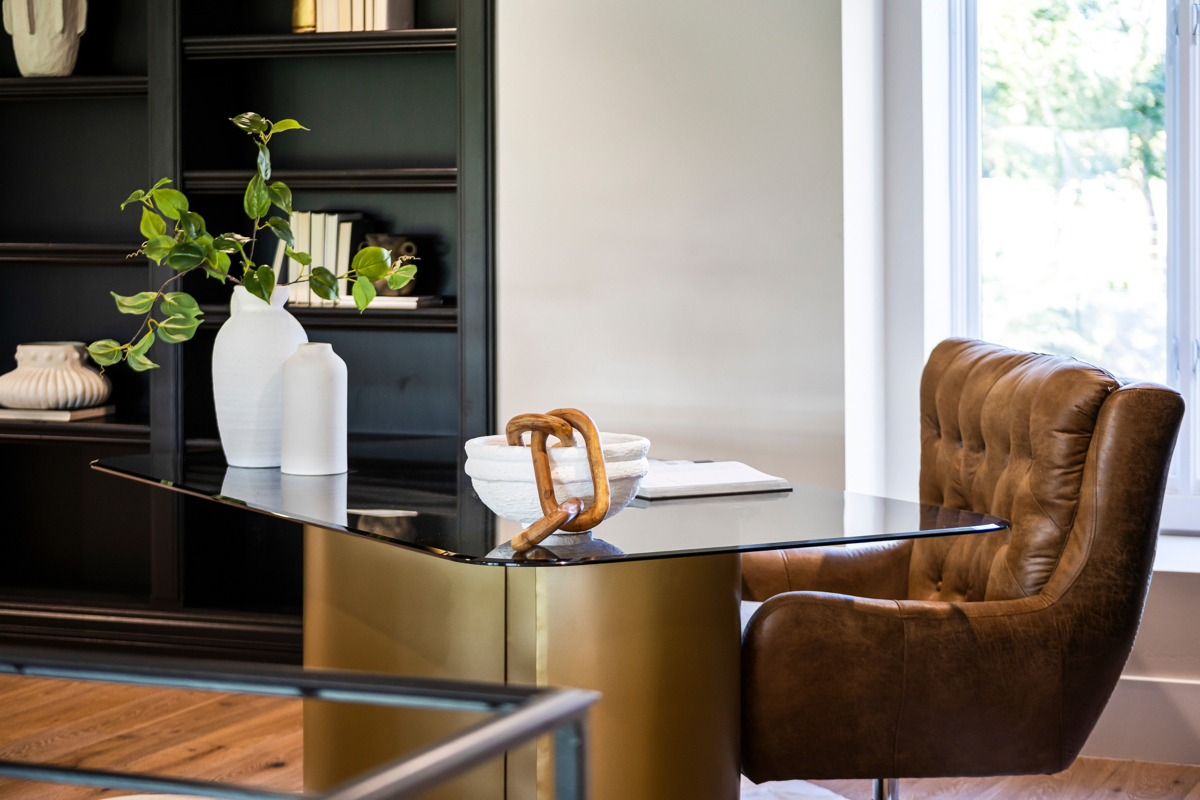Photo of a luxury home office featuring a black and gold desk, tufted brown leather chair, built-in shelving, and elegant décor.