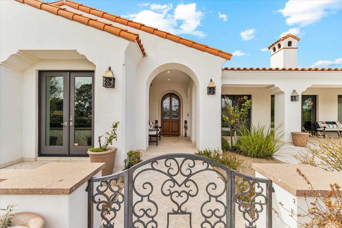 Photo of a Mediterranean-style luxury home with white stucco, terracotta roof tiles, an arched entrance, and decorative wrought-iron gates.