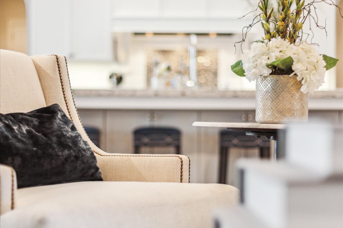 Elegant cream upholstered chair with a black accent pillow beside a floral arrangement in a luxury living room.