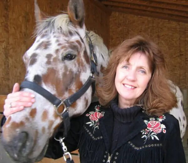 Rita Lovell standing beside a white Appaloosa horse