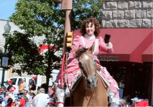 Rita Lovell in a pink dress riding a horse in a parade