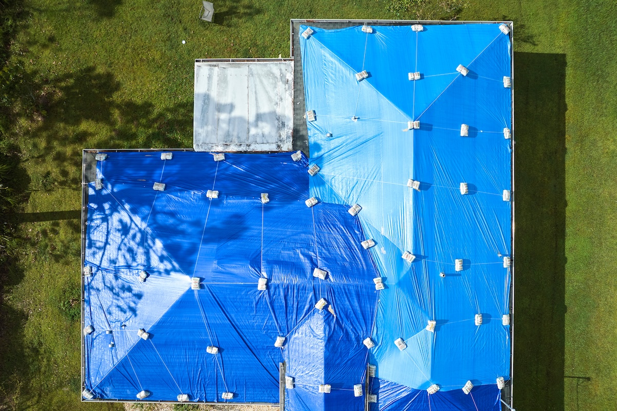 Top view of leaking house roof covered with protective tarp sheets against rain water leaks until replacement of asphalt shingles. Damage of building rooftop