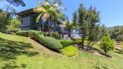 Modern Malibu hillside home surrounded by lush landscaping and palm trees, representing the costs of property upkeep and maintenance.