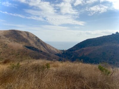 View from Solstice Canyon in Malibu overlooking the Pacific Ocean between two sunlit hills.
