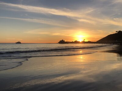 Golden sunset over Malibu Pier with waves gently rolling onto the beach.