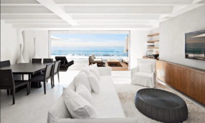 Bright Malibu beachfront living room opening to ocean deck with white sofa, dining table, and coastal view — ideal luxury rental interior.